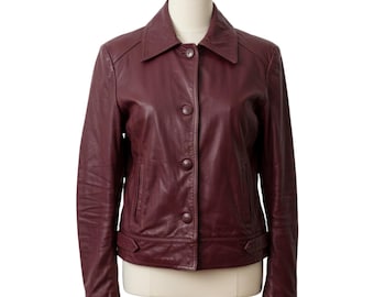 Puede incluir: Chaqueta de cuero burdeos con cuello clásico y cierre de botones. La chaqueta tiene dos bolsillos delanteros y un corte entallado. La chaqueta se muestra en un maniquí sobre un fondo blanco.
