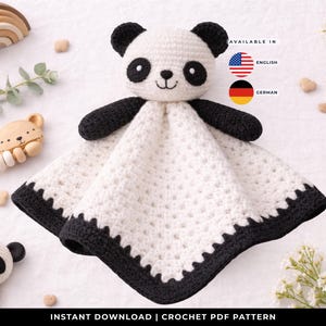 Könnte beinhalten: Eine gehäkelte Panda-Kuscheldecke mit weißem Körper und schwarzen Akzenten. Der Panda hat schwarze Ohren, Augen und Arme. Die Decke hat einen gewellten schwarzen Rand. Weitere Holzspielzeuge für Babys sind im Hintergrund.