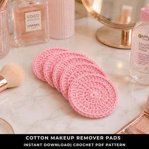 May include: A stack of five circular, light pink crocheted cotton makeup remover pads. The pads feature a textured, hand-stitched pattern with a consistent round shape and a finished edge, arranged in a slightly overlapping row on a white surface.