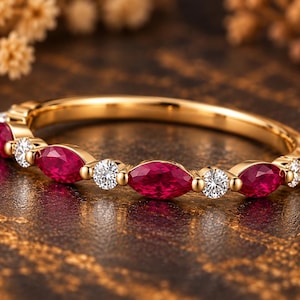 May include: A gold band ring featuring an alternating pattern of marquise-cut red rubies and round-cut white diamonds set in a continuous row along the top half of the metal band, showcasing a polished finish and vibrant gemstone colors.