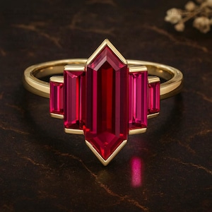 May include: A gold ring featuring a central, elongated, red gemstone flanked by four smaller, rectangular red gemstones. The ring has a geometric design with a polished gold band.