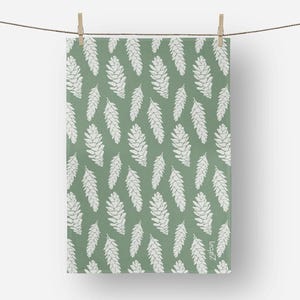May include: A green and white patterned kitchen towel featuring a repeating design of white pine cones. The towel is hanging from a clothesline with a wooden clothespin. The bottom right corner has the text "zaba".