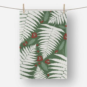 May include: A green and white fern pattern tea towel hanging from a clothesline. The design features white fern leaves and red berries on a green background. The towel is held by two wooden clothespins.