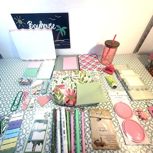 May include: A collection of stationery items including a floral patterned pouch, various pens, sticky notes, a pink glass tumbler with a lid, a small notebook, a wish bracelet on a card, and a decorative sign with the text Bayhouse.