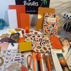 May include: A collection of stationery and accessories featuring orange and autumn-themed items. Included are notebooks, a word search book, a zippered pouch with the text hello fall, pens, a reading list notepad, stickers, and a leaf-shaped keychain.
