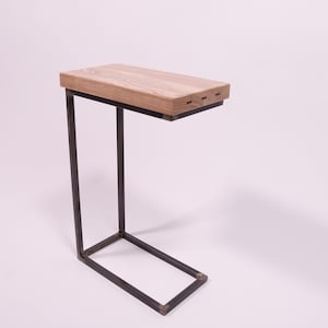 Op de afbeelding: Een bijzettafel met een rechthoekig licht houten blad en een donker metalen frame. Het tafelblad is 45 cm lang en 30 cm breed. Het frame heeft een C-vormig ontwerp.