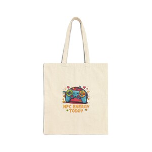 May include: Cream-coloured tote bag with a colourful cartoon gamepad design. The gamepad is blue, red, and green with the text "NPC ENERGY TODAY". The bag has a simple design with long handles.