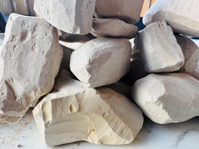 May include: A pile of irregularly shaped, light beige chalk rocks. The chalk pieces have rough, textured surfaces and varying sizes, with visible cut marks. The overall arrangement suggests a natural, raw material.