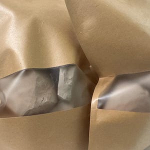 May include: Two brown paper bags with clear plastic windows, partially revealing the contents. The bags are sealed and appear to be filled with a light-colored, possibly granular, substance. The bags are sitting on a light-colored surface.