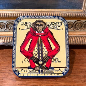 Peut inclure: Un jouet éducatif en métal vintage intitulé The Educated Monkey représentant un singe en manteau rouge. Le jouet a une face crème avec des chiffres noirs et des tables de multiplication. Deux bras en métal pointent vers des chiffres sur une base.
