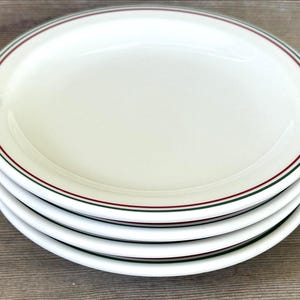 Könnte beinhalten: Ein Stapel von vier weißen Keramikplatten. Jede Platte hat einen dünnen roten und grünen Rand um den Rand. Die Platten sind übereinander gestapelt, wobei die oberste Platte nach oben zeigt.