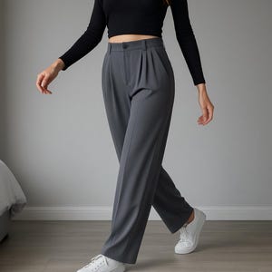 May include: Gray pleated trousers with a button closure, paired with a black long-sleeve top and white sneakers. The pants have a high waist and a straight leg design, creating a classic and versatile look.