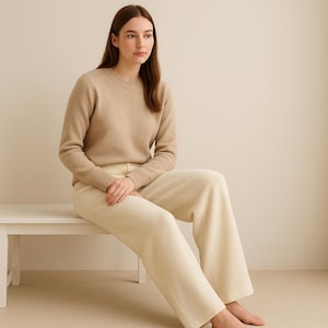 May include: A beige crew neck sweater and cream-colored wide-leg pants. The sweater has ribbed cuffs and a ribbed hem. The pants are high-waisted and have a relaxed fit. The outfit is simple and elegant, perfect for casual wear.