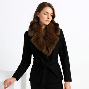 May include: A black coat featuring a brown fur collar and a matching waist belt. The coat has long sleeves and a classic design, suitable for cold weather. The fur collar adds a touch of luxury and warmth.
