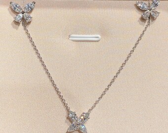 May include: A silver necklace and earring set featuring butterfly designs. The necklace has a butterfly pendant, and the earrings are butterfly studs. The jewelry is displayed in a beige box with a black frame.