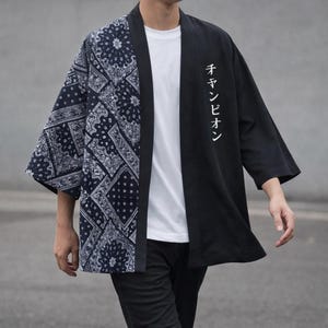 Op de afbeelding: Zwart-witte kimono-jas. Eén kant heeft een paisley-patroon, de andere is effen zwart met Japanse tekst. De jas heeft wijde mouwen en een relaxte pasvorm. Kledingstuk in Japanse stijl.