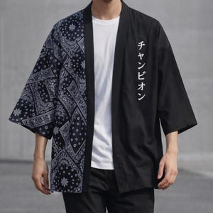 May include: Black and navy blue kimono-style jacket. The left side features a navy blue paisley pattern, while the right side is solid black with white Japanese text. The jacket has three-quarter sleeves and a relaxed fit.
