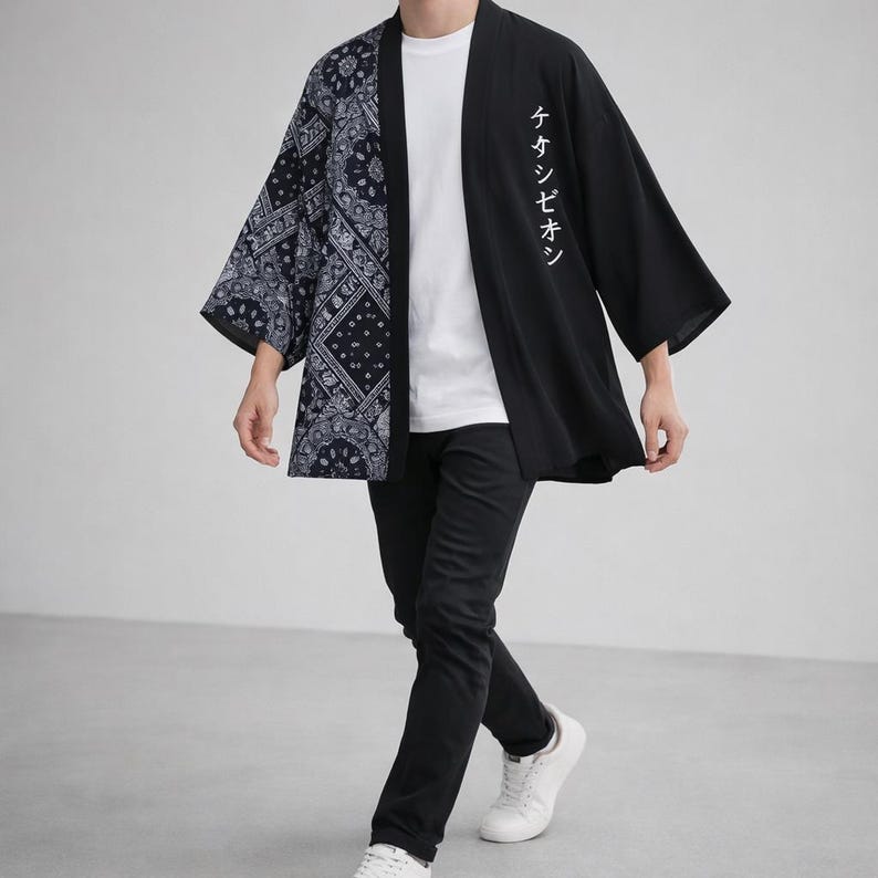 May include: Black and navy blue kimono-style jacket with a paisley pattern on the left side and Japanese text on the right. The jacket is worn over a white t-shirt and black pants. The person is wearing white sneakers.