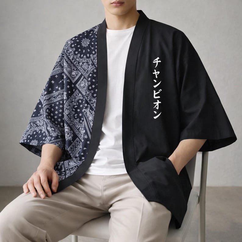 May include: Black and navy blue kimono-style jacket. The left side features a navy blue paisley pattern, while the right side is solid black with white Japanese text. The jacket has wide sleeves and is open in the front.