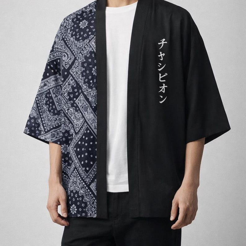 May include: Black and navy blue kimono-style jacket. The left side features a navy blue paisley pattern, while the right side is solid black with white Japanese text. The jacket has wide sleeves and a relaxed fit.