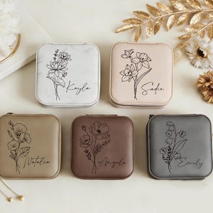 Może przedstawiać: Kolekcja kwadratowych etui na biżuterię w różnych kolorach, każdy ozdobiony kwiatowym wzorem i imieniem w skrypcie. Etui posiadają zapięcie na zamek błyskawiczny i są ułożone na jasnej powierzchni. Kwiatowe ilustracje są czarne.