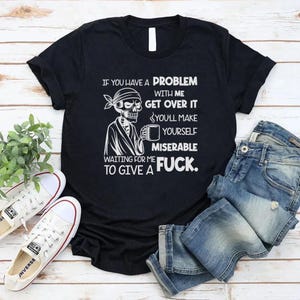 May include: Black t-shirt with a white graphic of a skeleton wearing a bandana and holding a mug. The shirt has the text: "If you have a problem with me, get over it. You'll make yourself miserable waiting for me to give a fuck."