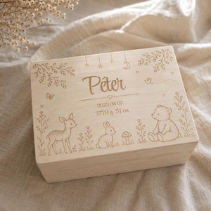 May include: A rectangular light-coloured wooden keepsake box featuring laser-engraved illustrations of a fawn, a rabbit, a teddy bear, and foliage. The lid is inscribed with the name Péter, the date 2023.04.07, and the birth stats 3770 g and 51 cm.