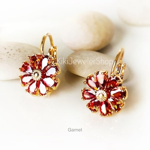 May include: Gold-coloured flower earrings with red and white gemstones. The earrings have a lever back closure. The word "Garnet" is printed at the bottom of the image. The earrings are displayed on a white surface.
