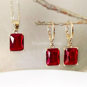 May include: A gold-toned necklace with a rectangular, deep red pendant, and matching lever-back earrings. The jewelry set features a bright, polished finish. The image includes the text "KikiJewelShop".