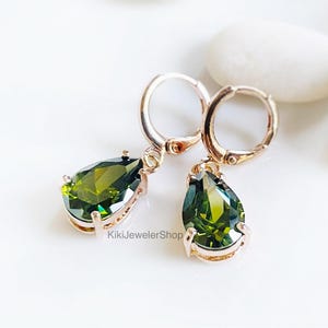 Op de afbeelding: Rosegouden oorringen met peer-vormige olijfgroene edelstenen. De oorbellen worden gepresenteerd op een witte ondergrond. De oorbellen zijn van KikiJewelerShop.
