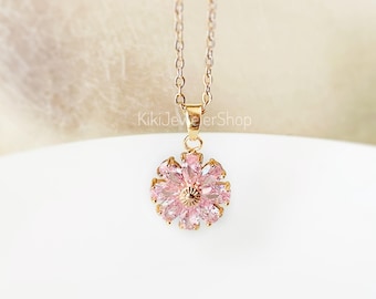 May include: A rose gold necklace with a pendant shaped like a flower. The flower pendant is made of pink gemstones and has a gold center. The necklace is displayed on a white surface.