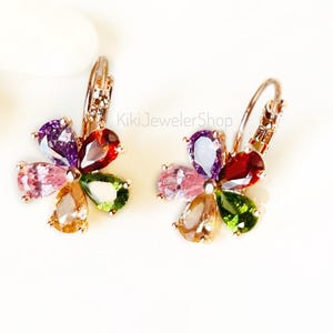 Pode incluir: Um par de brincos em forma de flor com pedras preciosas coloridas. Cada brinco apresenta seis pedras em forma de gota em tons de roxo, vermelho, rosa, verde, laranja e amarelo. Os brincos têm acabamento em ouro rosa e fecho de pressão.