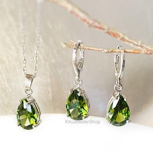 Op de afbeelding: Een zilveren ketting met een peervormige groene edelsteen hanger en een paar bijpassende oorbellen. De oorbellen en hanger zijn gezet in zilver metaal. De sieraden worden gepresenteerd op een lichte achtergrond.