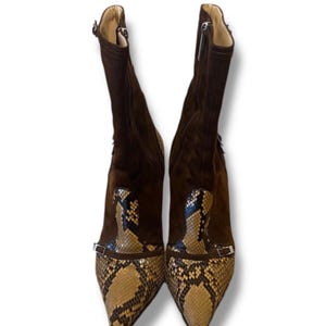 Peut inclure: Une paire de bottines en daim marron avec des bouts pointus et un motif peau de serpent sur l'empeigne. Les bottines ont un talon haut et une fermeture éclair latérale. Un petit détail de boucle est présent.