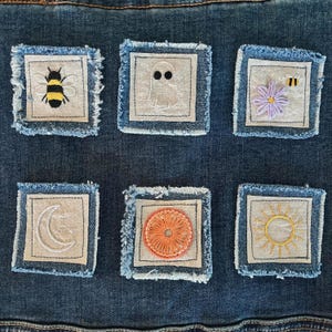Peut inclure: Six écussons brodés avec divers motifs, dont une abeille, un fantôme, une fleur avec une abeille, un croissant de lune, un cercle orange et un soleil. Chaque écusson est carré, avec un motif brodé de couleur claire sur un carré de tissu, bordé de denim.
