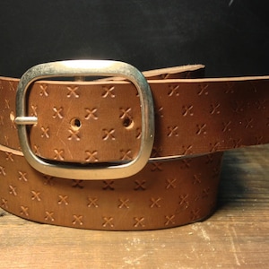 May include: A brown leather belt with a silver buckle. The belt has a repeating pattern of small crosses embossed into the leather.