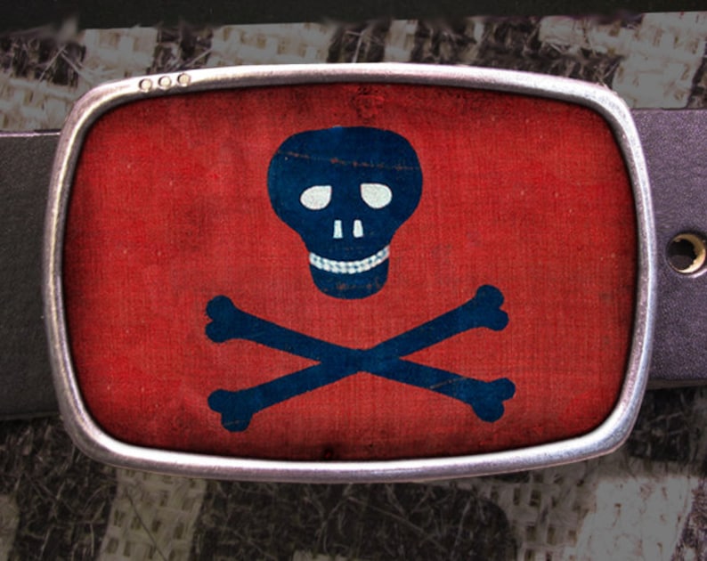 May include: A silver belt buckle with a red background and a blue skull and crossbones design.