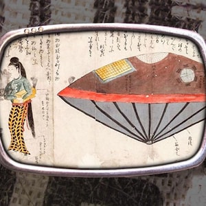 May include: A silver belt buckle with a vintage illustration of a flying saucer and a woman in traditional Japanese clothing. The illustration is surrounded by Japanese text.