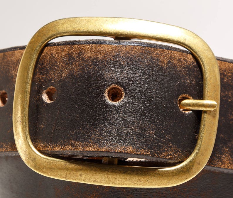 May include: A distressed brown leather belt with a brass buckle. The buckle is a simple oval shape with a smooth finish.