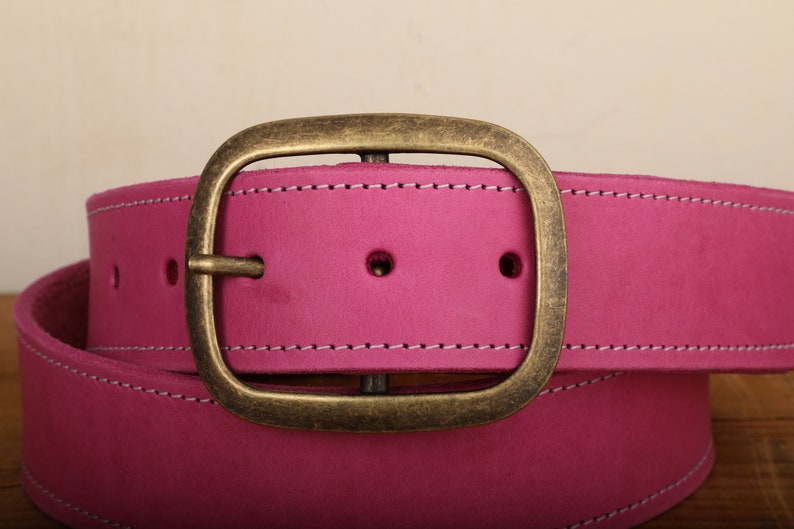 May include: A pink leather belt with a brass buckle. The belt has white stitching around the edges.