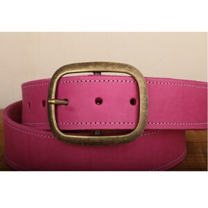 May include: A pink leather belt with a brass oval buckle. The belt has white stitching around the edges.