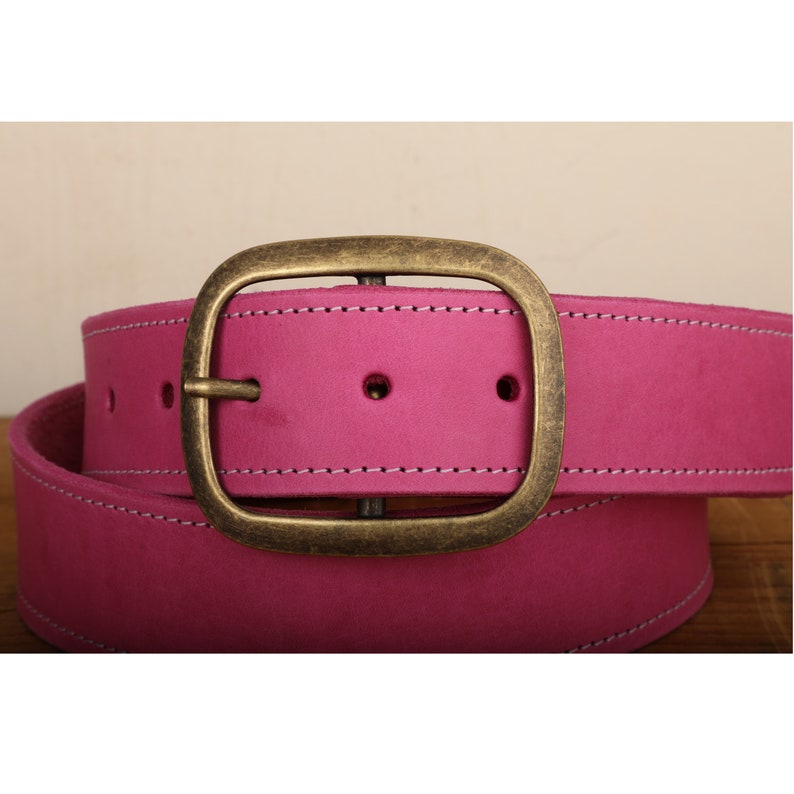 May include: A pink leather belt with a brass oval buckle. The belt has white stitching around the edges.