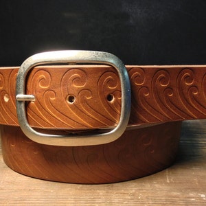 May include: A brown leather belt with a silver buckle. The belt has a wave pattern embossed into the leather.