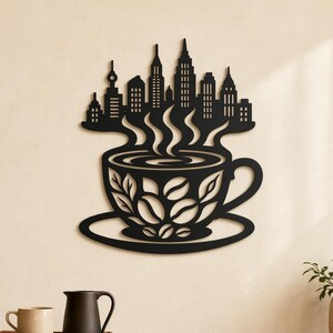 Pode incluir: Uma peça de arte de parede em metal preto com a silhueta de uma chávena de café com um horizonte urbano a surgir do vapor. A chávena é decorada com um padrão de grãos de café e o design é feito a partir de uma única folha de metal.