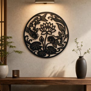 以下が含まれることがあります： 黒い金属製の円形ウォールアート。レーザーカットされた2匹の鯉が中央の蓮の花の周りを泳ぎ、睡蓮の葉と渦巻く水の模様が描かれています。木製のベンチの上に設置されています。
