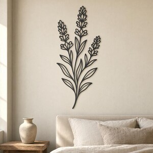 Può includere: Un'opera d'arte da parete in metallo nero raffigurante un design floreale stilizzato. L'opera presenta uno stelo centrale con più foglie e tre grappoli di fiori. Il pezzo è montato su una parete di colore neutro, creando un'estetica minimalista.
