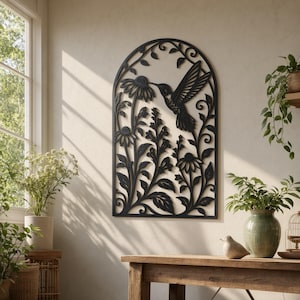 May include: A black arched wall art piece featuring a laser-cut design of a hummingbird hovering near flowers and foliage. The intricate metal or wood cutout displays a detailed silhouette of the bird and various botanical elements.