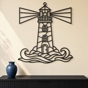 May include: Black metal lighthouse wall art. The lighthouse features a detailed design with windows, a door, and stylized waves at the base. The lighthouse has a light beam extending from the top. A blue vase sits on a black cabinet.