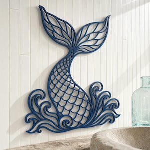 Può includere: Decorazione murale a forma di coda di sirena blu navy con un design a onde. La coda di sirena è intagliata con un motivo a scaglie e una pinna dettagliata. La decorazione è montata su una parete bianca con assi verticali.