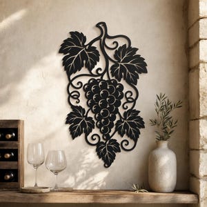 Può includere: Un'opera d'arte da parete in metallo nero che presenta una silhouette dettagliata di un grappolo d'uva con viticci ricci e foglie seghettate. Il design è intricato e mostra un grappolo centrale circondato da fogliame per un effetto decorativo.